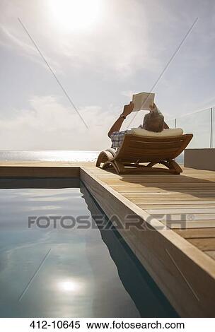 Stock Photography - Man reading in lawn chair by pool. Fotosearch