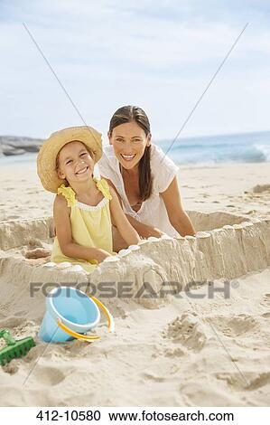 Stock Image - Mother and daughter making sandcastle on beach. Fotosearch