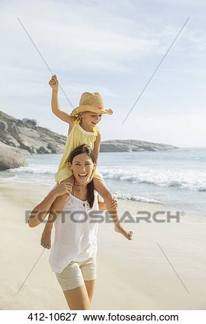 Stock Photo - Mother carrying daughter on shoulders on beach. Fotosearch