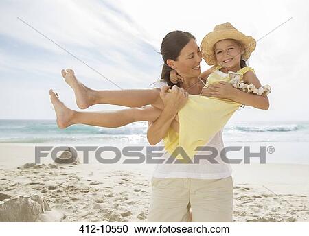 Stock Image - Mother holding daughter on beach. Fotosearch