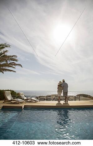 Stock Image - Older couple hugging by pool. Fotosearch