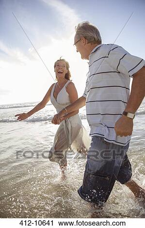 Older couple playing in waves on beach View Large Photo Image Stock Image - Older couple playing in waves on beach. Fotosearch