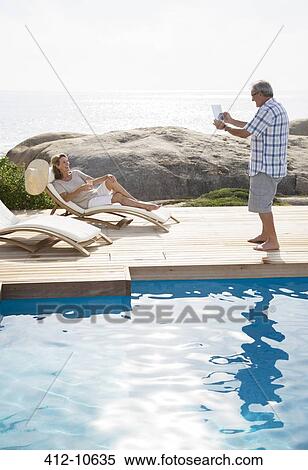 Stock Photography - Older man taking picture of girlfriend by pool. Fotosearch