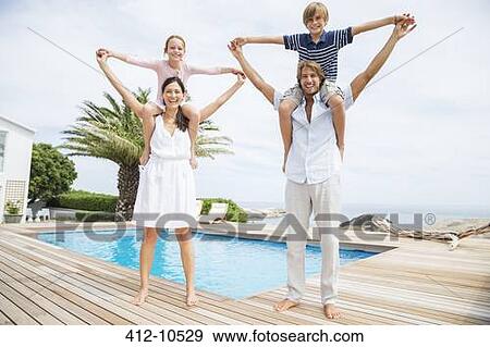 Stock Photo - Parents carrying children on shoulders at luxury poolside. Fotosearch