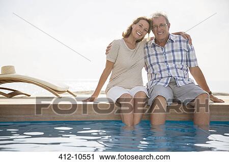 Stock Image - Senior couple dipping feet in swimming pool. Fotosearch