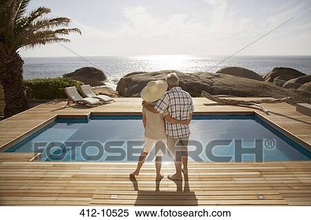 Stock Photography - Senior couple hugging by modern pool overlooking ocean. Fotosearch