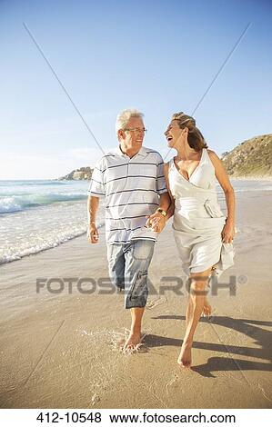 Senior couple walking in surf on beach View Large Photo Image Stock Photo - Senior couple walking in surf on beach. Fotosearch