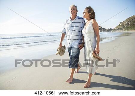 Stock Image - Senior couple walking on beach. Fotosearch