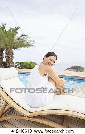 Stock Photo - Woman relaxing in lawn chair by pool. Fotosearch
