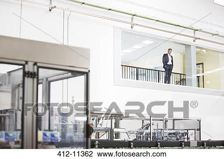 Businessman in window overlooking factory View Large Photo Image Stock Image - Businessman in window overlooking factory. Fotosearch