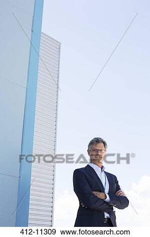 Stock Photo - Businessman standing below highrise buildings. Fotosearch