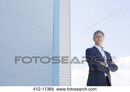 Businessman standing below highrise buildings View Large Photo Image Stock Photography - Businessman standing below highrise buildings. Fotosearch
