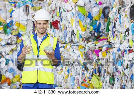 Stock Image - Worker holding compacted plastic bottle in recycling center. Fotosearch