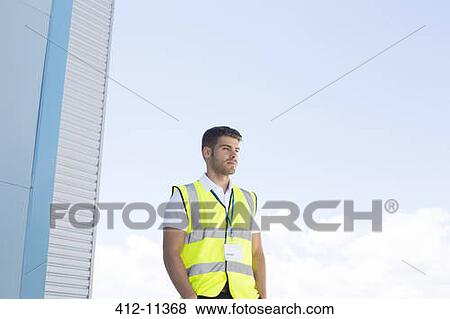 Stock Photo - Worker standing below highrise building. Fotosearch