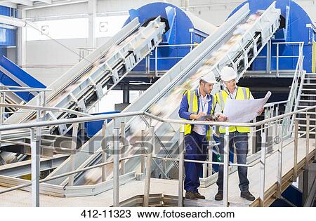 Stock Image - Workers reading blueprints in recycling center. Fotosearch