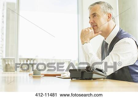 Stock Image - Businessman sitting at desk in office. Fotosearch