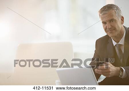 Businessman using cell phone and laptop in office View Large Photo Image Stock Image - Businessman using cell phone and laptop in office. Fotosearch
