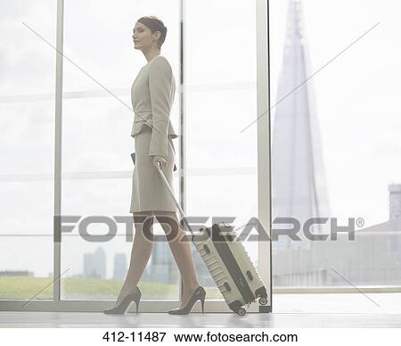 Stock Photo - Businesswoman rolling suitcase in airport. Fotosearch