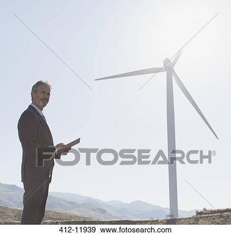 Businessman admiring wind turbine in rural landscape View Large Photo Image Stock Photo - Businessman admiring wind turbine in rural landscape. Fotosearch