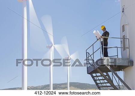 Businessman examining blueprints by wind turbines in rural landscape View Large Photo Image Picture - Businessman examining blueprints by wind turbines in rural landscape. Fotosearch