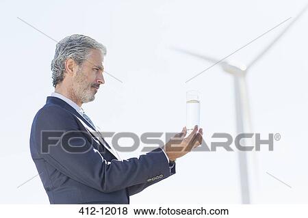 Businessman examining glass of water by wind turbine View Large Photo Image Stock Photo - Businessman examining glass of water by wind turbine. Fotosearch