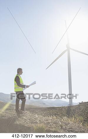 Stock Photo - Businessman examining wind turbine in rural landscape. Fotosearch