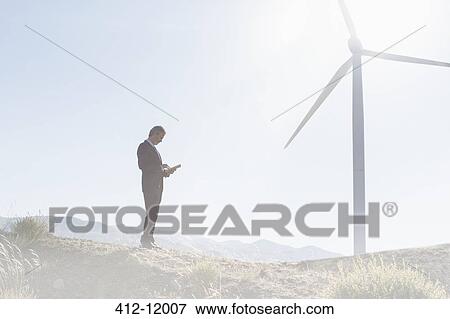 Businessman using laptop by wind turbine in rural landscape View Large Photo Image Stock Photo - Businessman using laptop by wind turbine in rural landscape. Fotosearch