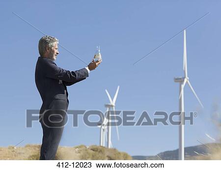 Businessman with glass of water by wind turbines in rural landscape View Large Photo Image Stock Image - Businessman with glass of water by wind turbines in rural landscape. Fotosearch