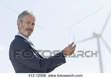 Businessman with glass of water by wind turbine View Large Photo Image Stock Photograph - Businessman with glass of water by wind turbine. Fotosearch