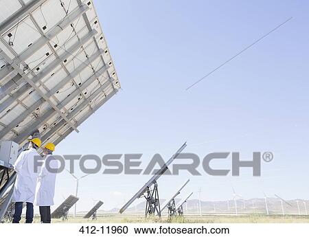 Stock Image - Scientists examining solar panel in rural landscape. Fotosearch