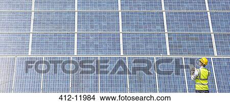 Picture - Worker examining solar panel in rural landscape. Fotosearch