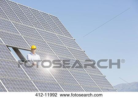 Stock Image - Worker examining solar panel in rural landscape. Fotosearch