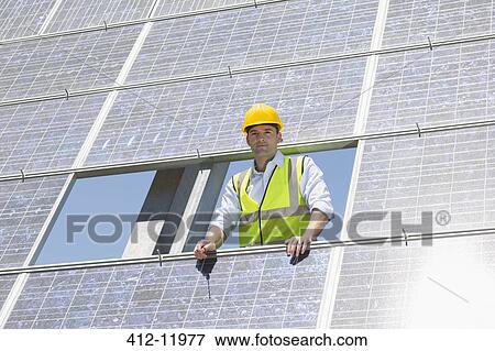 Stock Photo - Worker examining solar panel in rural landscape. Fotosearch