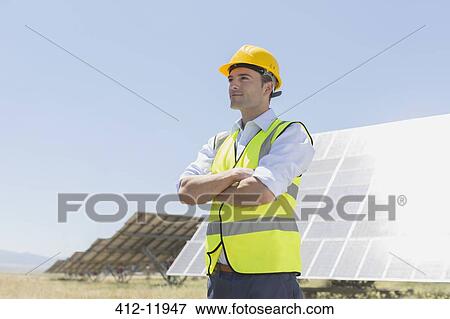 Stock Photo - Worker standing by solar panels in rural landscape. Fotosearch