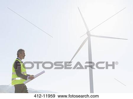 Worker standing by wind turbine in rural landscape View Large Photo Image Stock Photo - Worker standing by wind turbine in rural landscape. Fotosearch