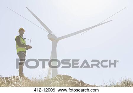 Stock Photography - Worker standing by wind turbine in rural landscape. Fotosearch