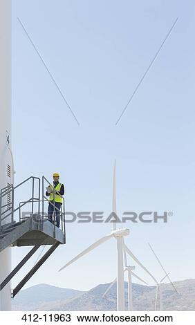 Stock Image - Worker standing on wind turbine in rural landscape. Fotosearch