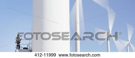 Stock Photo - Worker standing on wind turbine in rural landscape. Fotosearch