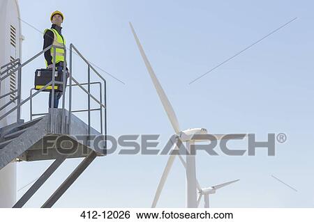 Worker standing on wind turbine in rural landscape View Large Photo Image Stock Photograph - Worker standing on wind turbine in rural landscape. Fotosearch