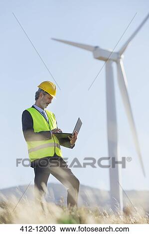 Worker using laptop by wind turbine in rural landscape View Large Photo Image Stock Image - Worker using laptop by wind turbine in rural landscape. Fotosearch