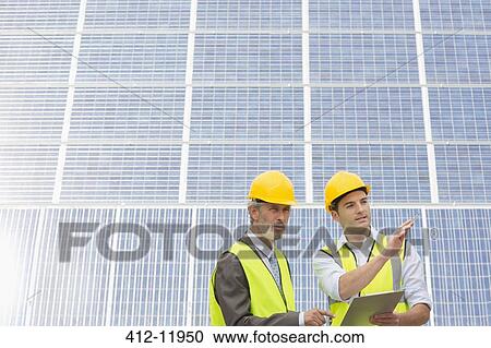 Workers examining solar panels in rural landscape View Large Photo Image Stock Image - Workers examining solar panels in rural landscape. Fotosearch