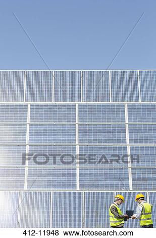 Workers examining solar panels in rural landscape View Large Photo Image Stock Photo - Workers examining solar panels in rural landscape. Fotosearch