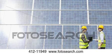 Workers examining solar panels in rural landscape View Large Photo Image Stock Photo - Workers examining solar panels in rural landscape. Fotosearch