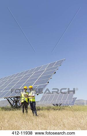 Workers standing by solar panels in rural landscape View Large Photo Image Stock Photo - Workers standing by solar panels in rural landscape. Fotosearch