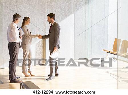 Business people shaking hands in sunny office lobby View Large Photo Image Picture - Business people shaking hands in sunny office lobby. Fotosearch