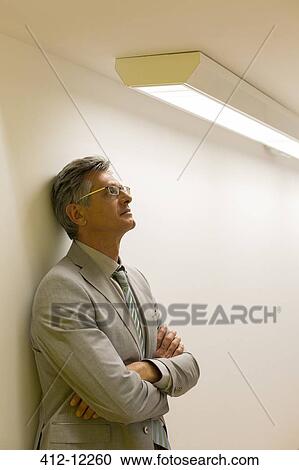 Stock Image - Businessman leaning against office wall. Fotosearch