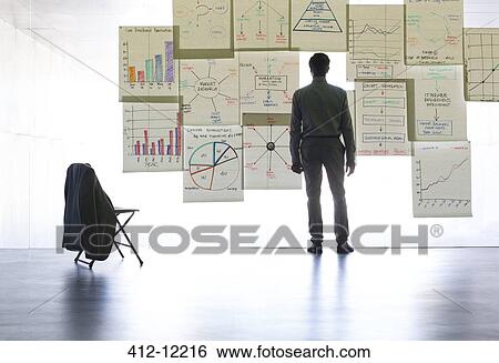 Businessman looking at graphs and charts on glass wall in office View Large Photo Image Stock Photograph - Businessman looking at graphs and charts on glass wall in office. Fotosearch