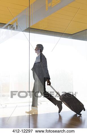 Stock Photo - Businessman pulling suitcase in airport corridor. Fotosearch