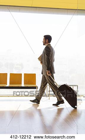 Stock Image - Businessman pulling suitcase in office. Fotosearch
