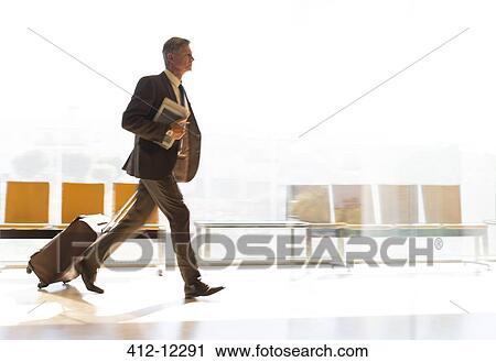 Stock Image - Businessman running with suitcase in airport corridor. Fotosearch